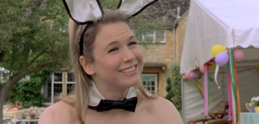 from the movie Bridget Jones Diary, character Bridget Jones stands outdoors at a party wearing black and white bunny ears and a bow tie.