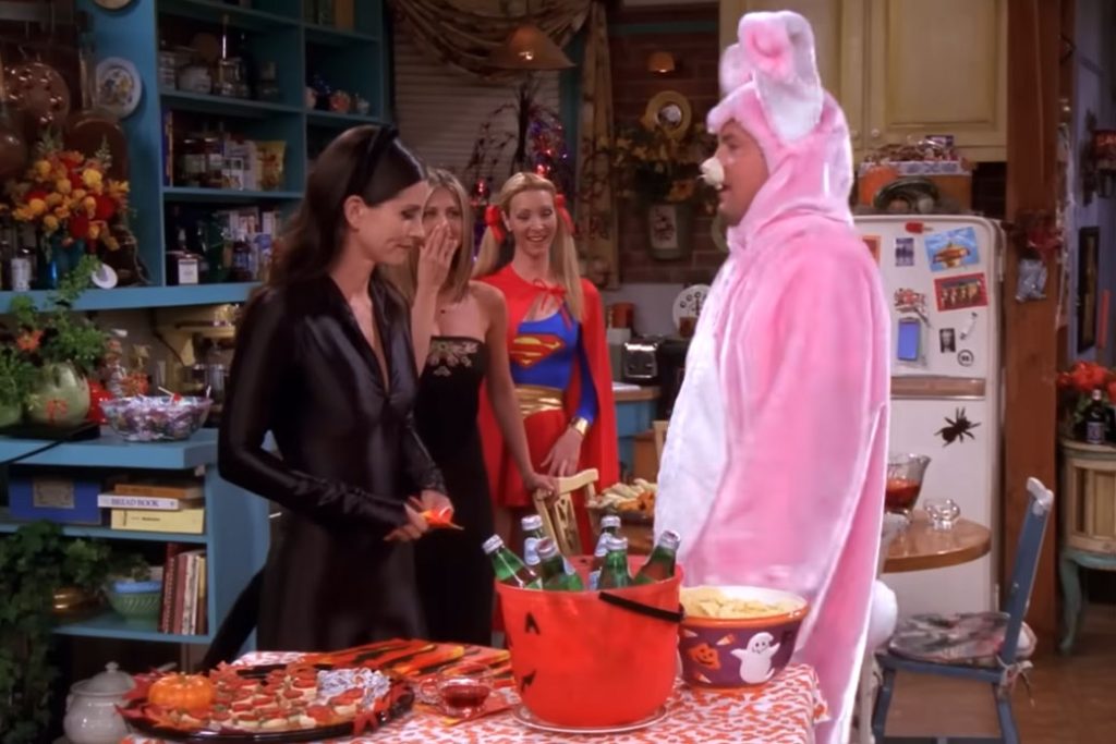 friends tv show characters stand around a table at a halloween party wearing costumes.