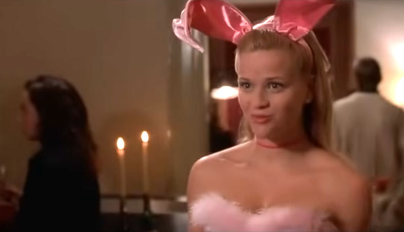 A young woman with blonde hair wears pink bunny ears and a feathery top.